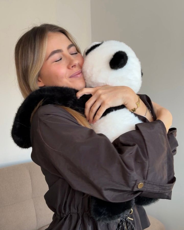 A young woman smiles with her eyes closed as she hugs Pookie the Panda