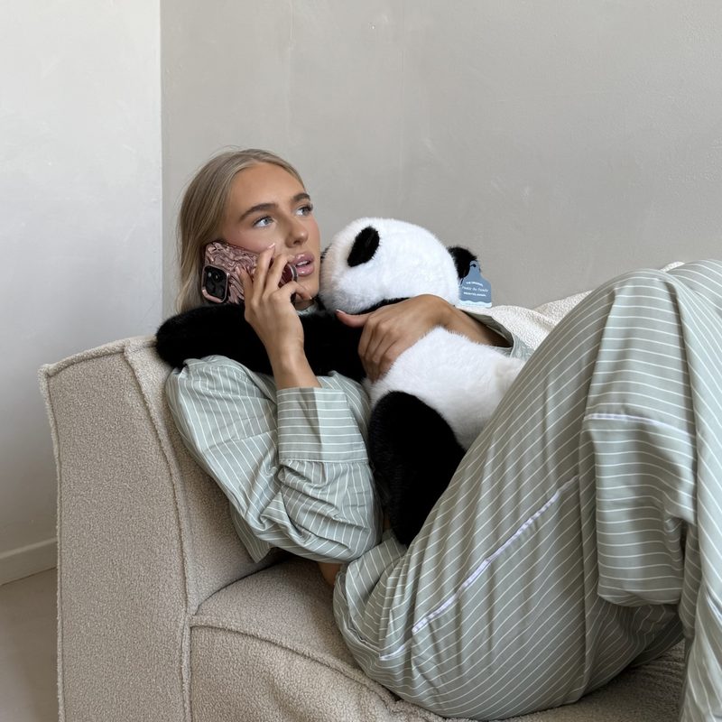 A young woman curls up on the couch with Pookie the Panda while she talks on the phone