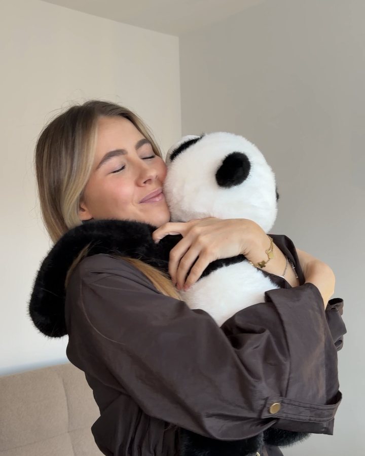 A young woman smiles with her eyes closed as she hugs a weighted panda, its long arms around her back
